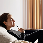 **Prompt:** A cozy, modern living room bathed in soft, ambient light. A person (e.g., a young woman, an elderly man) is comfortably interacting with a sleek, minimalist smart speaker or smartphone. Gentle, warm, glowing sound waves or auroras emanate from the device, subtly wrapping around the person, symbolizing AI voice transforming from cold data into a natural, emotionally expressive presence. The person's face shows a relaxed, engaged, and content expression, reflecting the seamless integration of AI voice into their daily life, making tasks easier and more personal. The scene evokes a sense of comfort, convenience, and the quiet magic of modern technology.